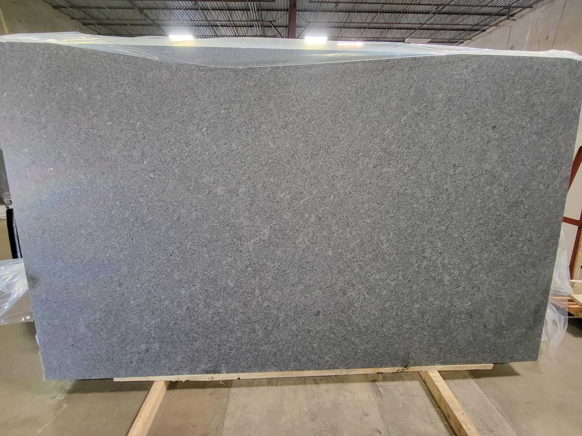 Large gray speckled stone slab on a pallet in a warehouse setting
