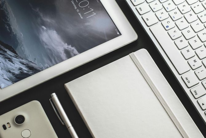 Tablette blanche, clavier, smartphone, ordinateur portable et stylo sur une surface sombre, suggérant un espace de travail.