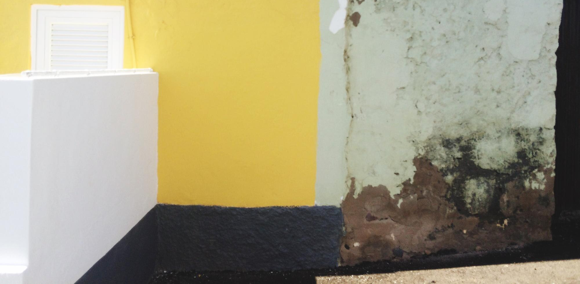 A yellow and white wall, meeting a weathered, mouldy wall with dark patches.