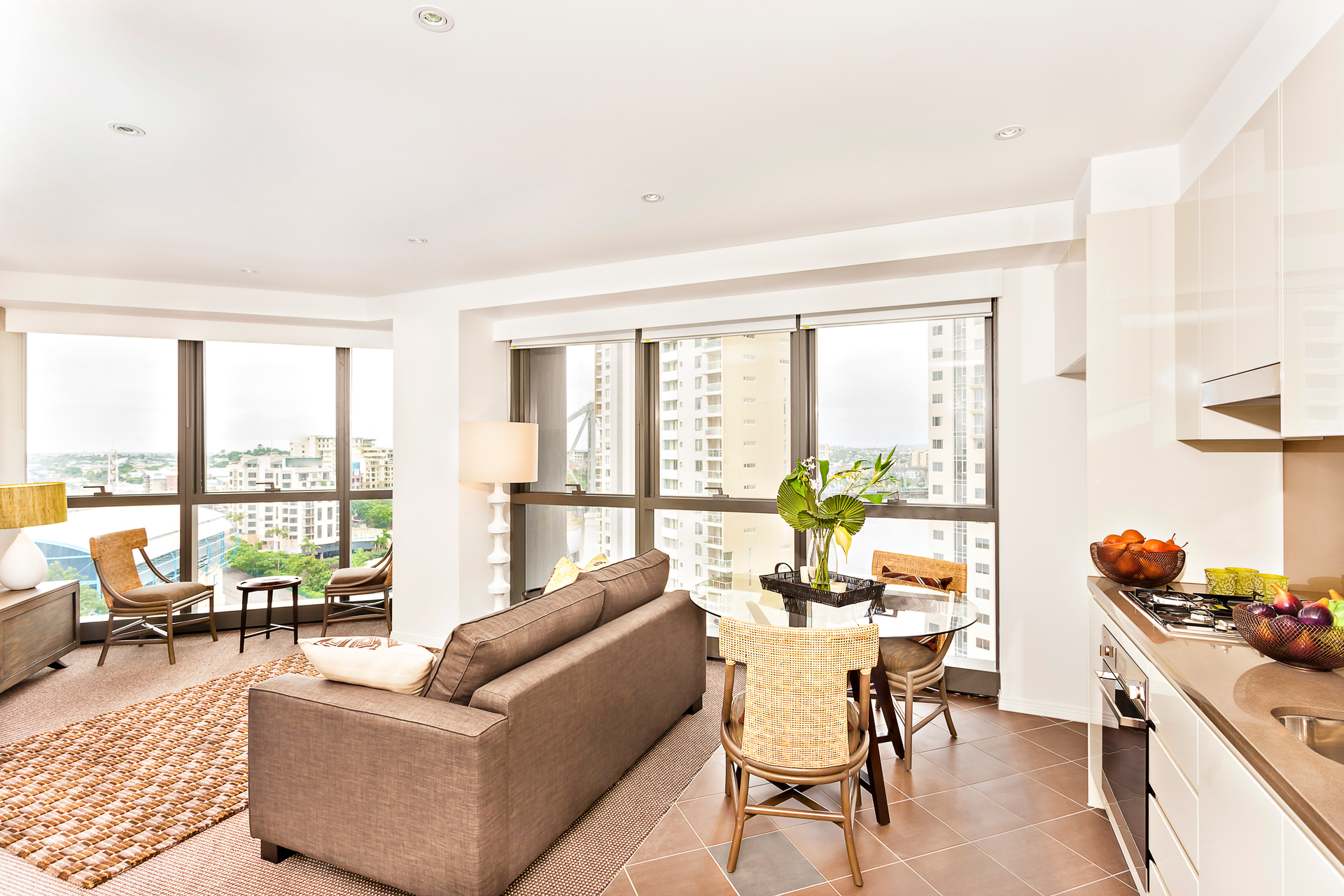 Bright living area with large windows, brown sofa, and small dining table.
