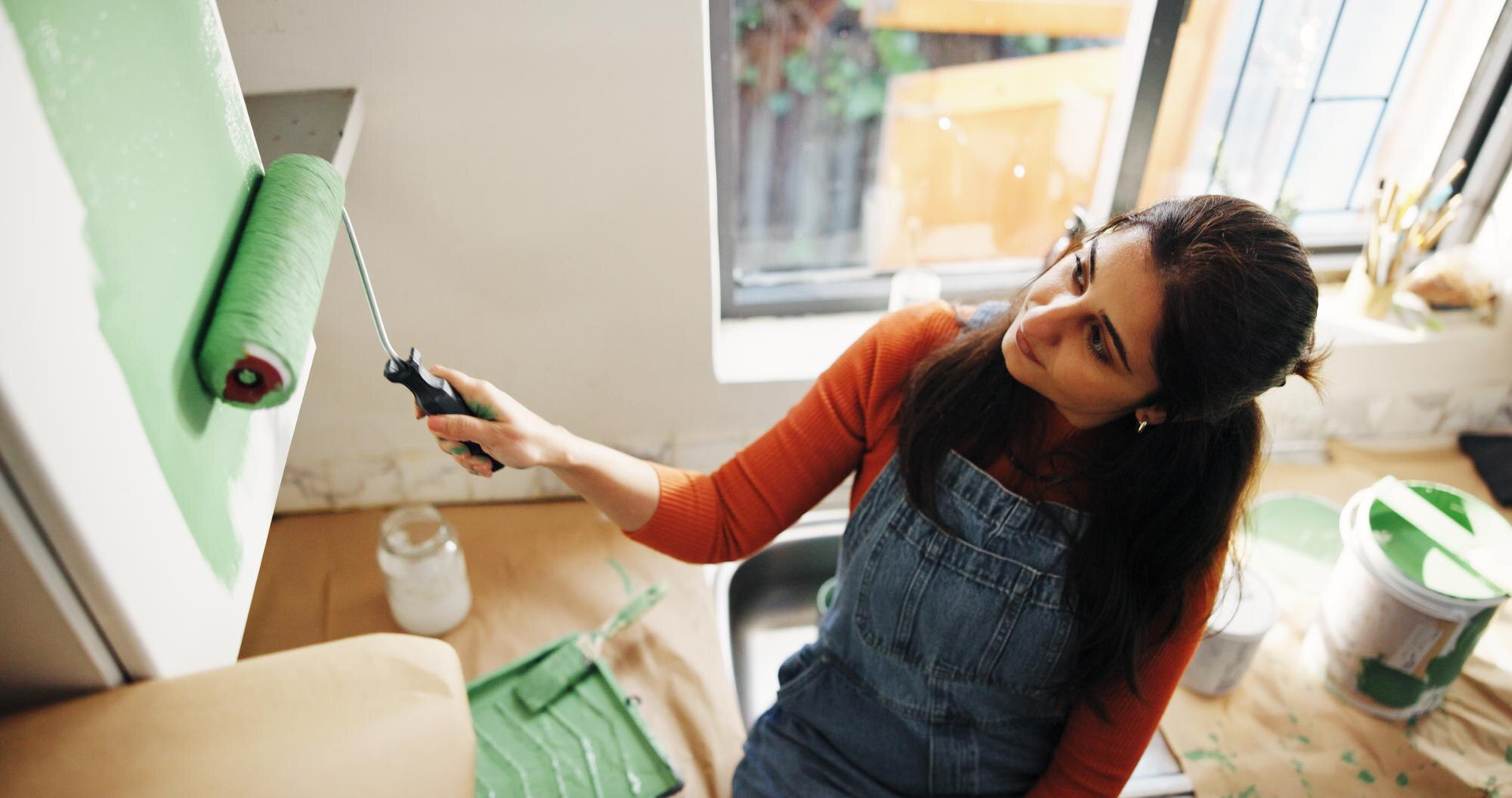 Woman paints canvas green with roller in bright room.