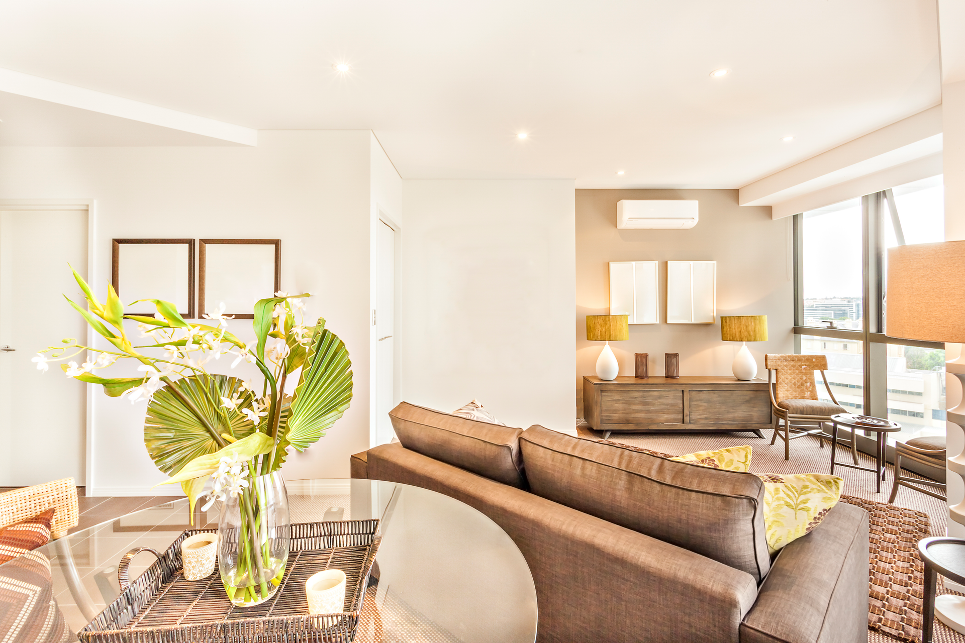 Living room with gray sofa, natural wood console, large windows, and flower arrangement.