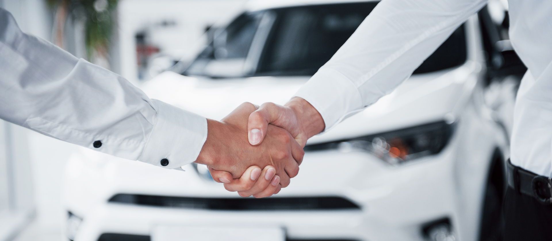 Two people are shaking hands in front of a white car.