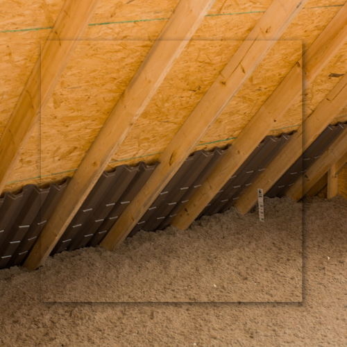 Attic interior with foam insulation on walls and rafters. Sunlight streams through a window.