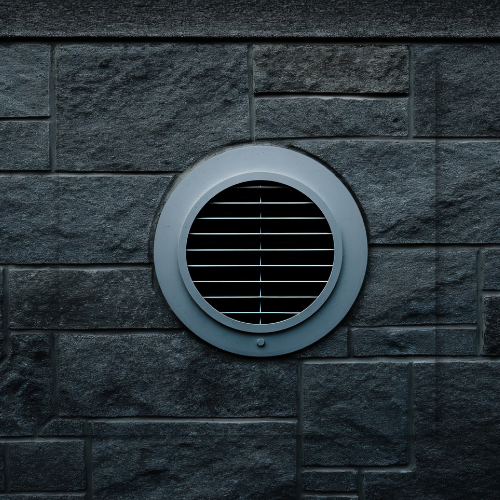 Gray circular vent on a dark gray brick wall.