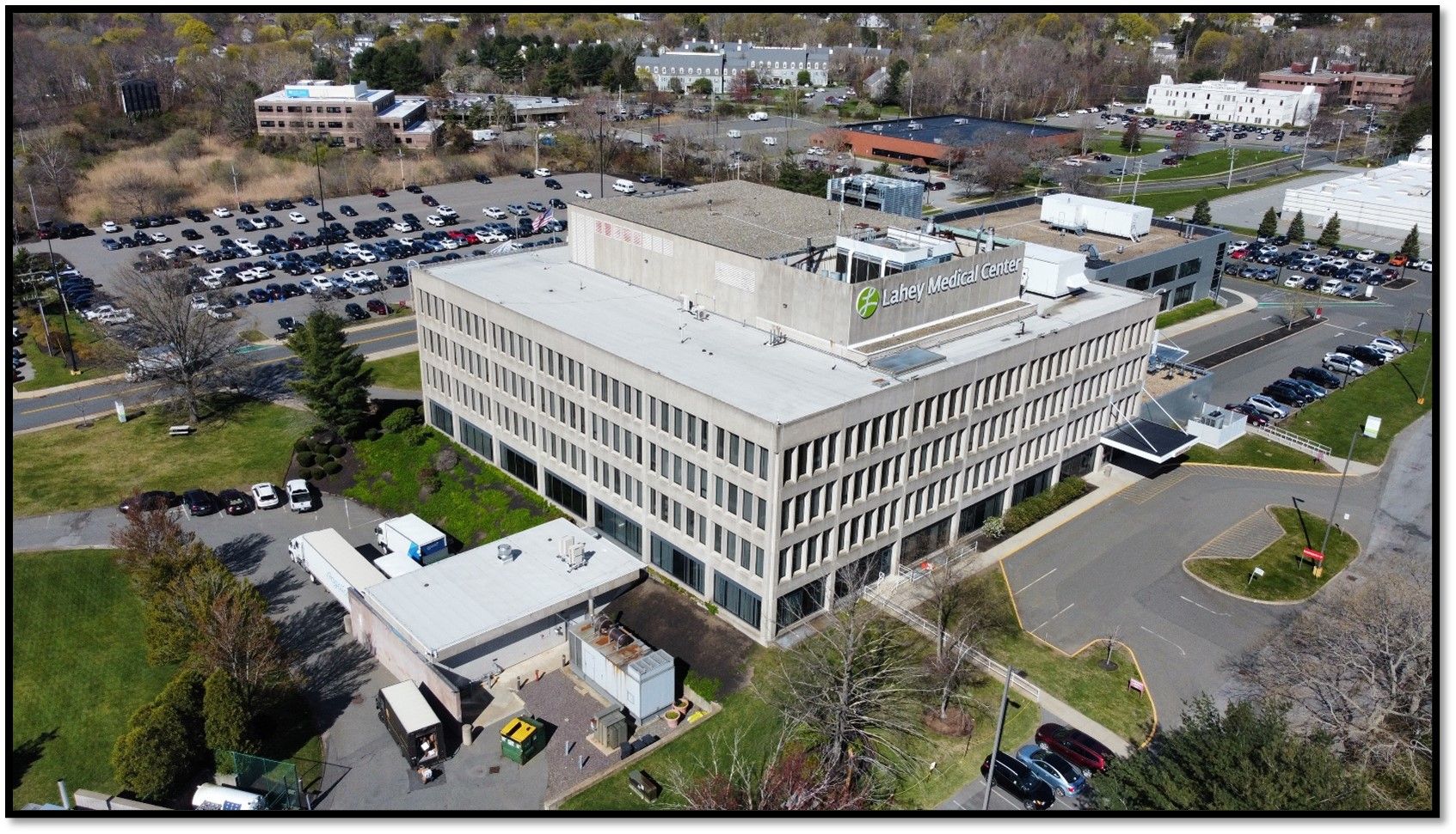 An aerial view of a multi-story office building with a flat roof, surrounded by parking lots and sparse trees.