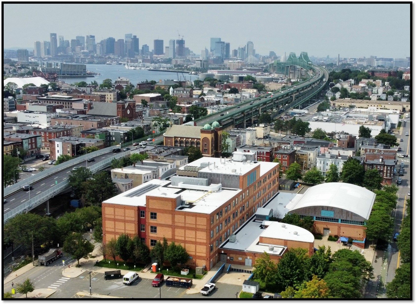 Aerial view of a school building with solar panels on the roof, surrounded by a playground, parking lot, and trees.