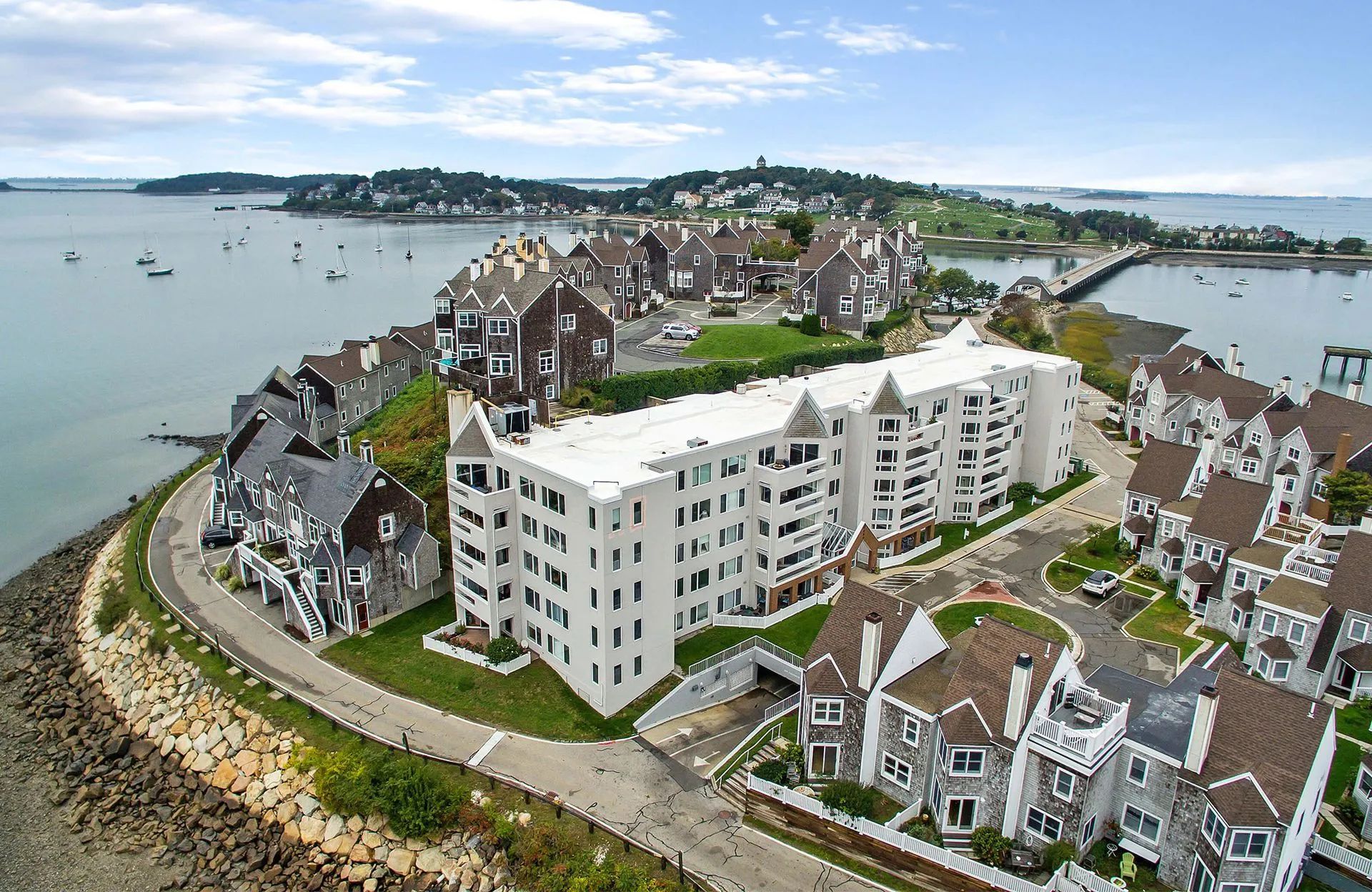Aerial view of a coastal condominium complex with white and gray buildings, green lawns, and a bridge.