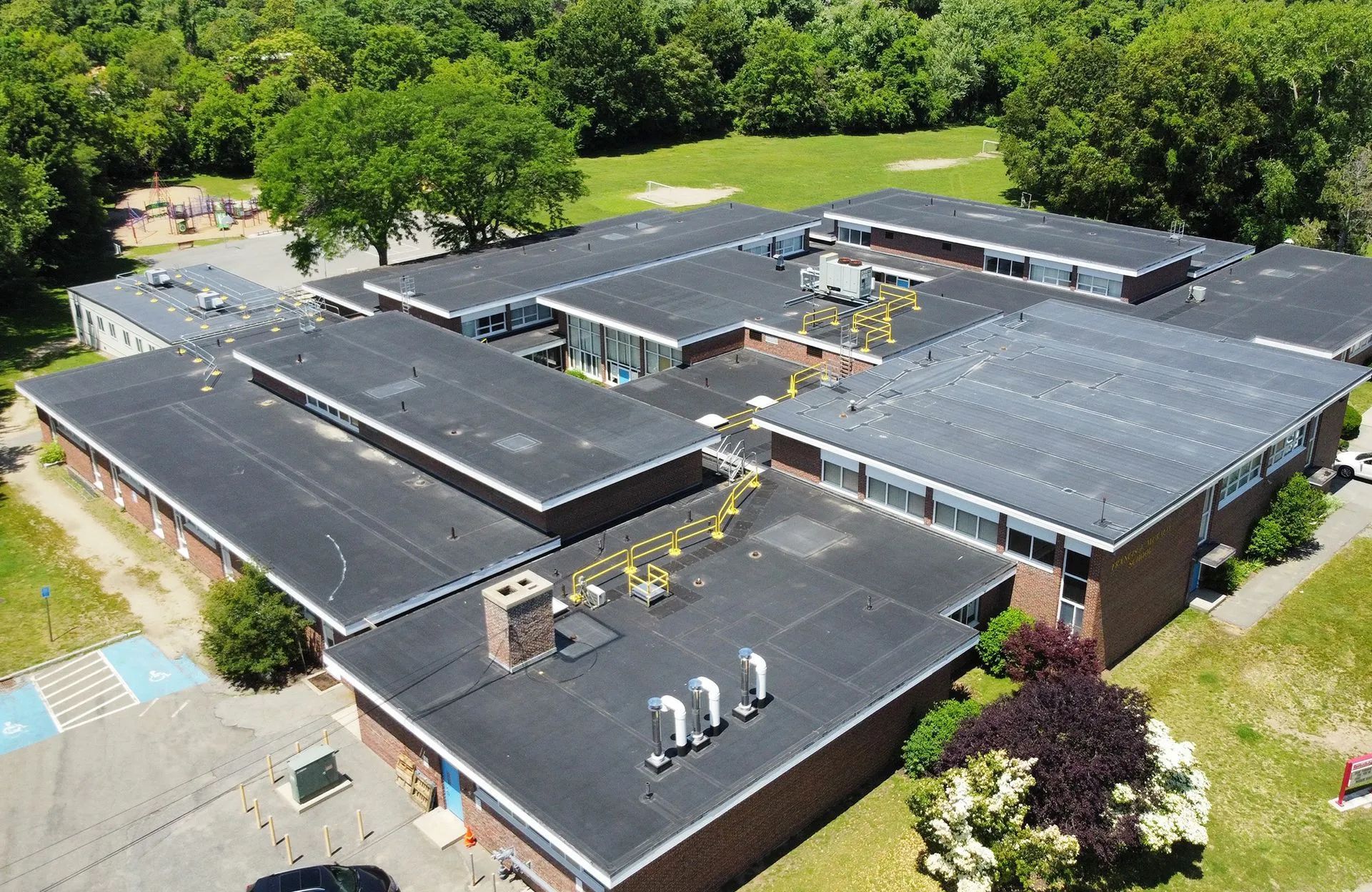 Overhead view of a school building with a flat black roof, surrounded by green trees and grass.