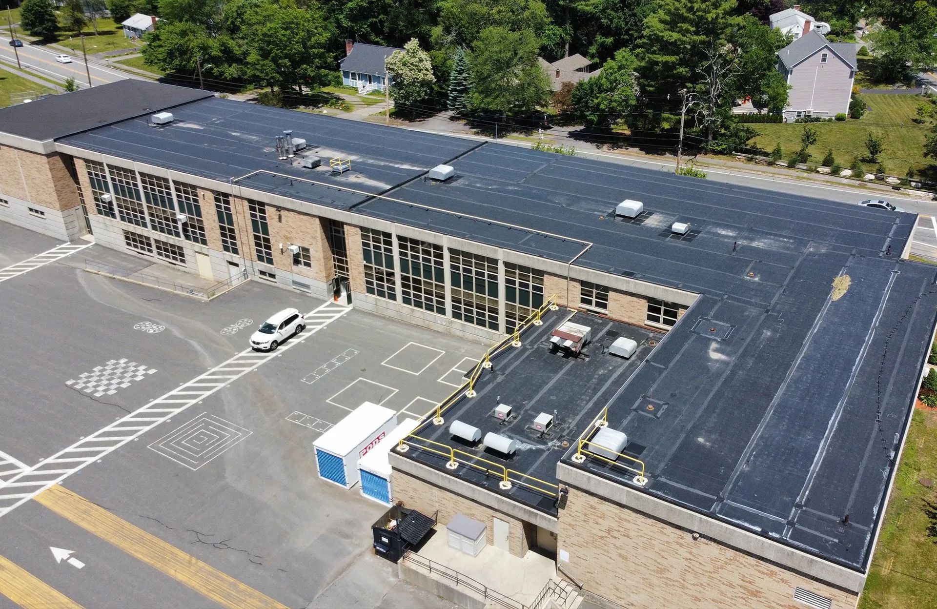 Aerial view of a long, brick building with a flat, black roof. A white van is parked in the lot.