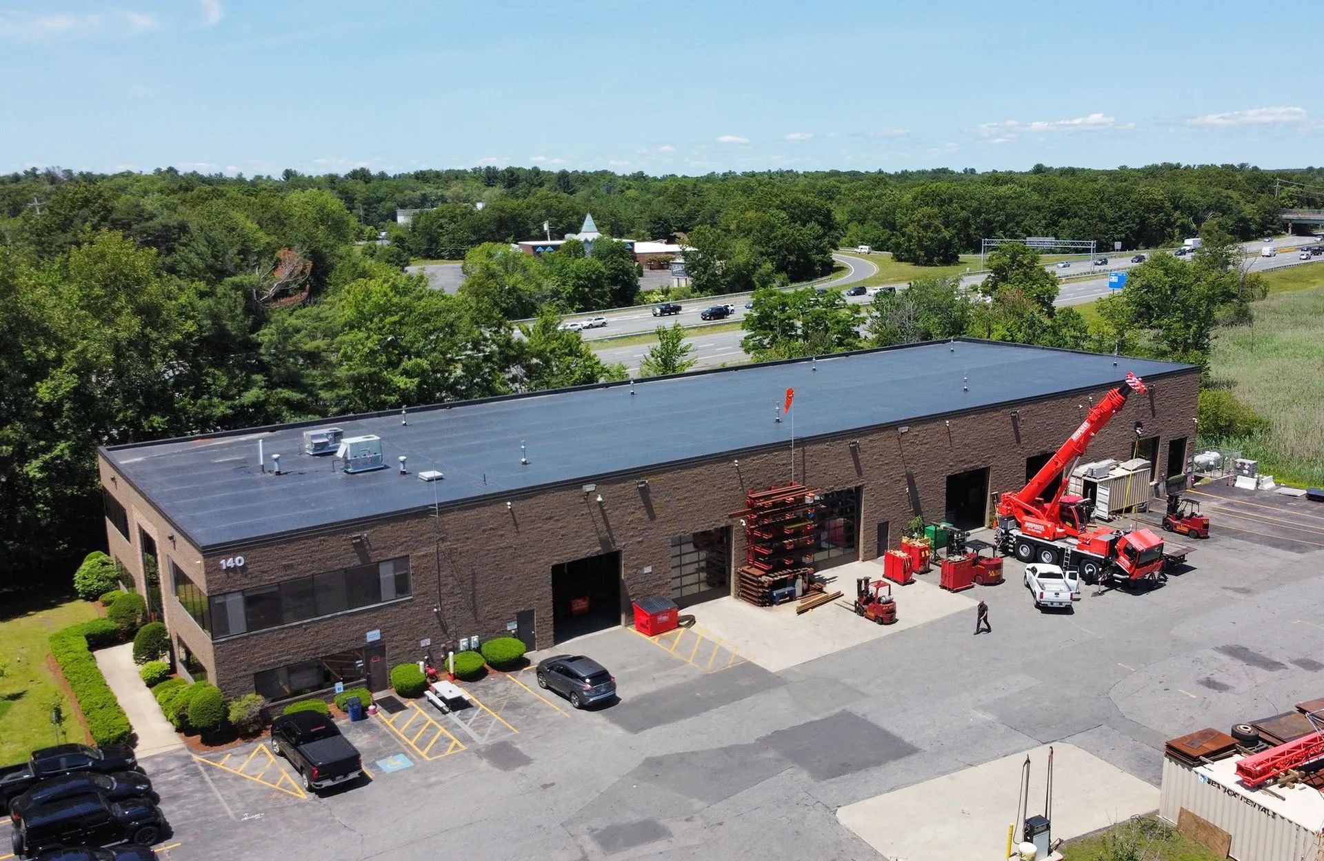 Aerial view of a brick industrial building with a crane and trucks on a sunny day.
