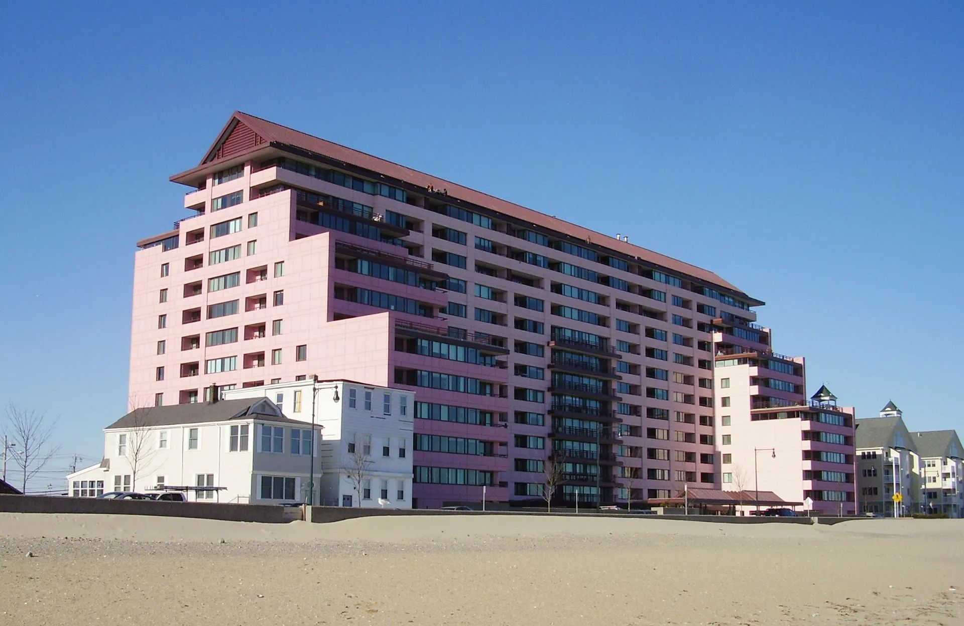 Large pink apartment building on a beach with a red roof, under a clear blue sky.