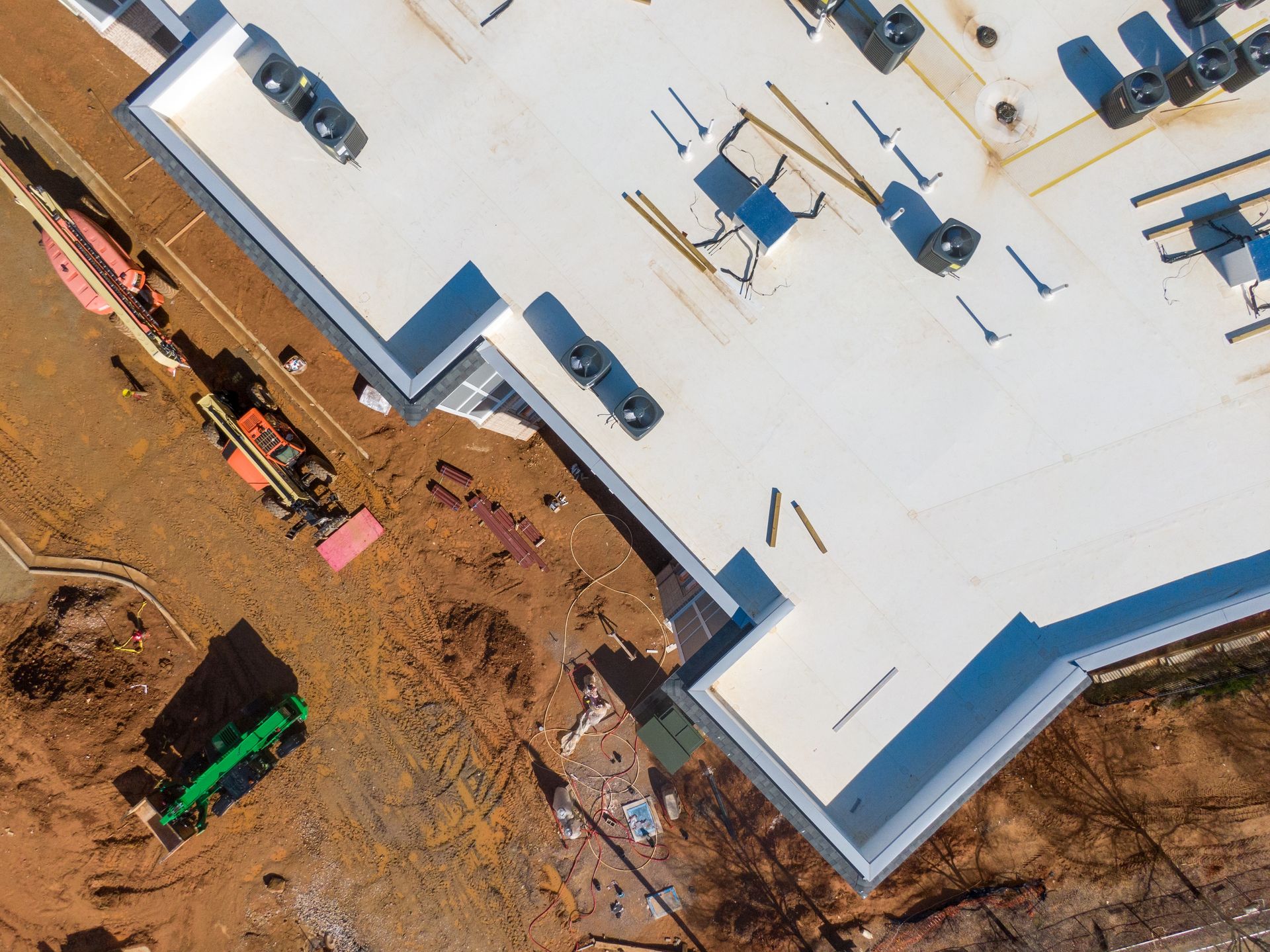 Aerial view of a white commercial roof under construction with HVAC units, surrounded by a dirt excavation site.