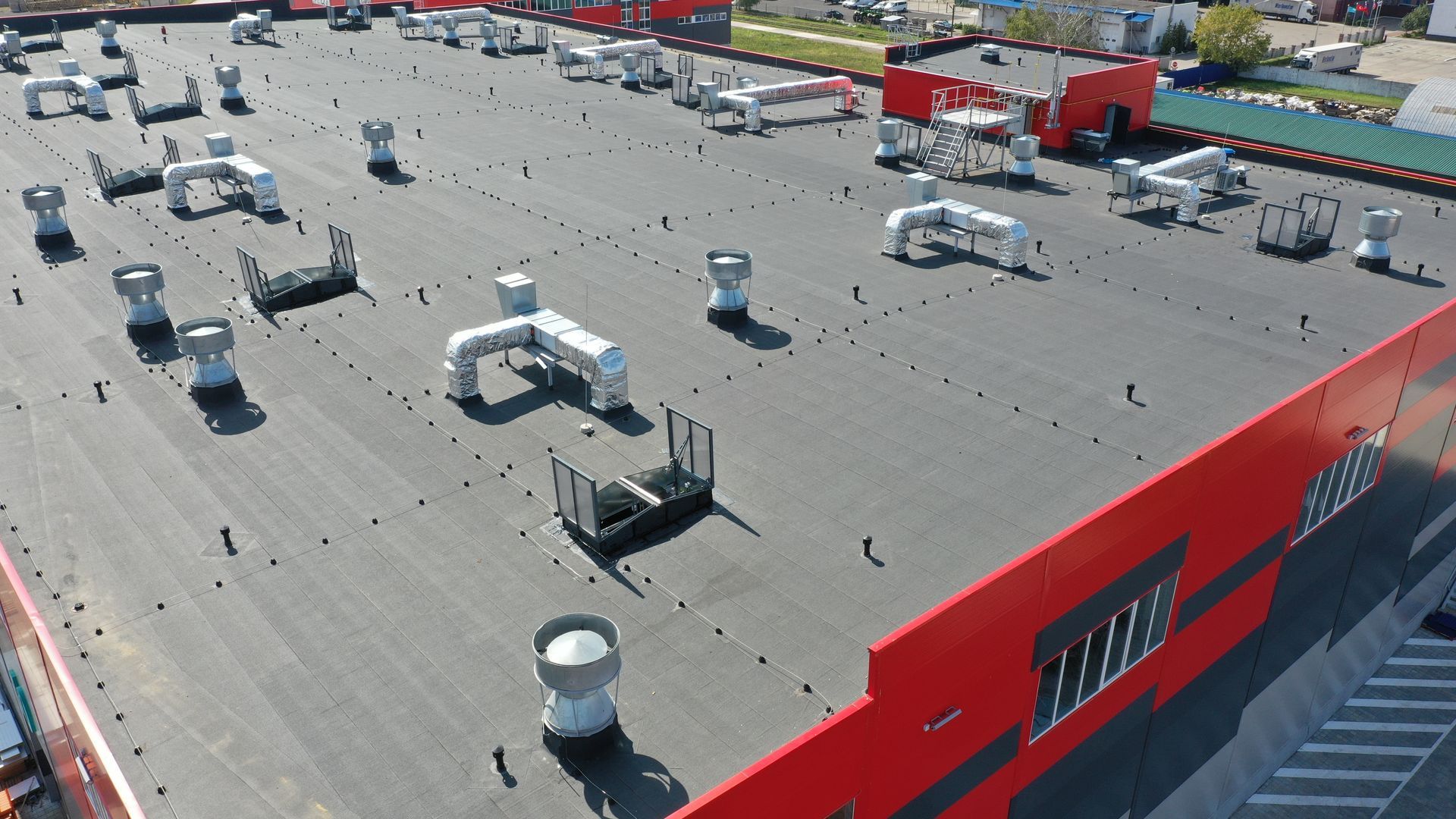 Aerial view of a flat, dark roof on a large building with red exterior walls and numerous HVAC ventilation units.