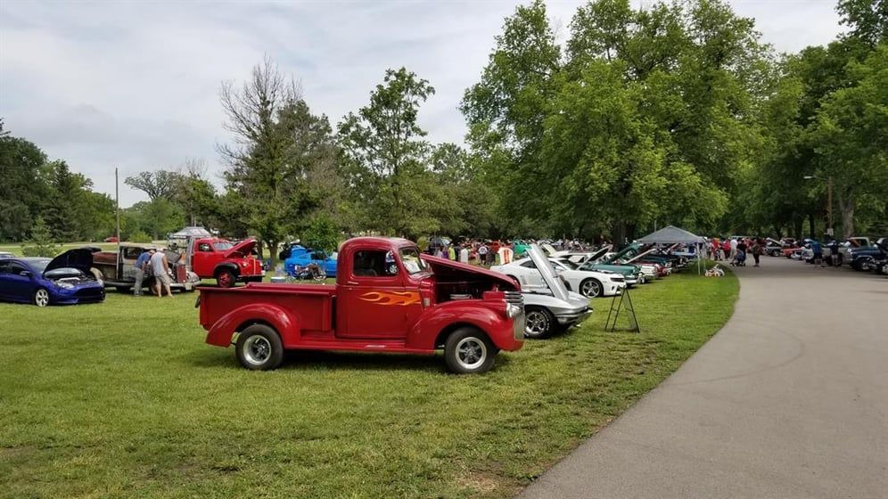 A red truck is parked in the grass at a car show.