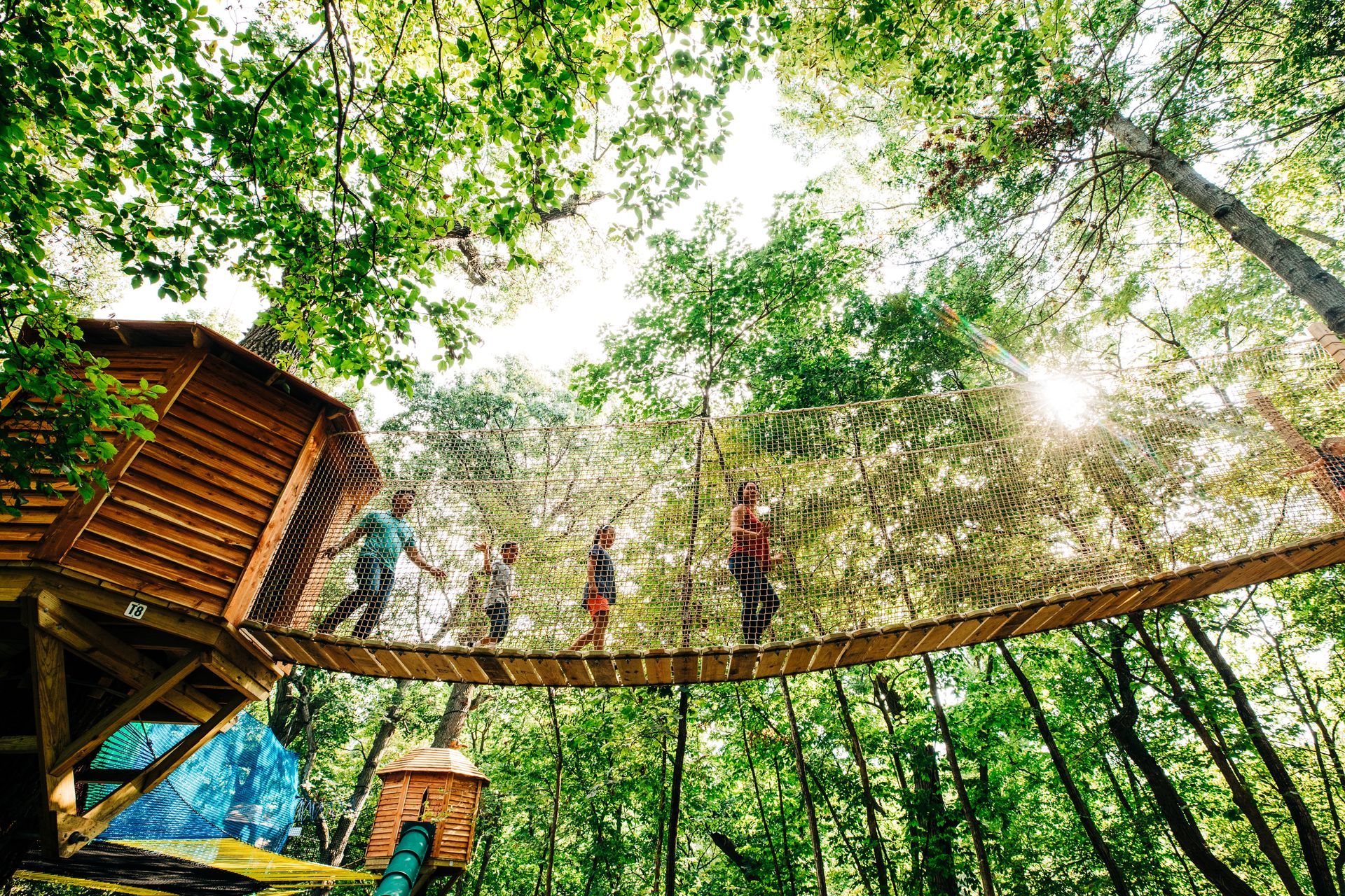 A group of people are walking across a wooden bridge in the woods.