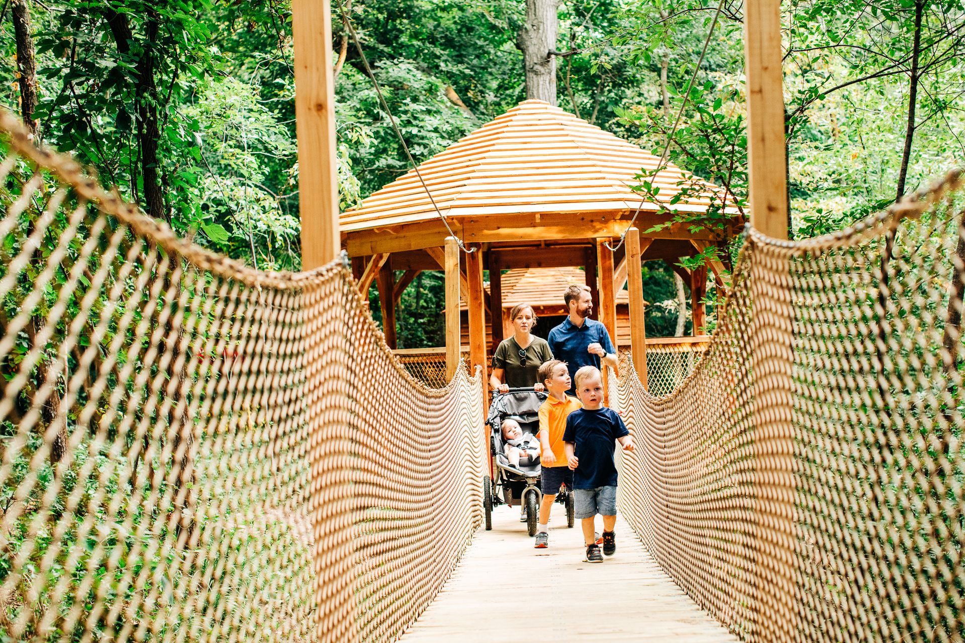 A family is walking across a rope bridge in the woods.