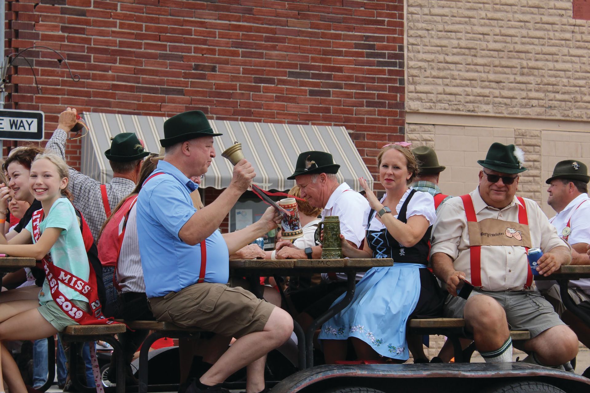 A group of people are sitting at a picnic table in front of a brick building.