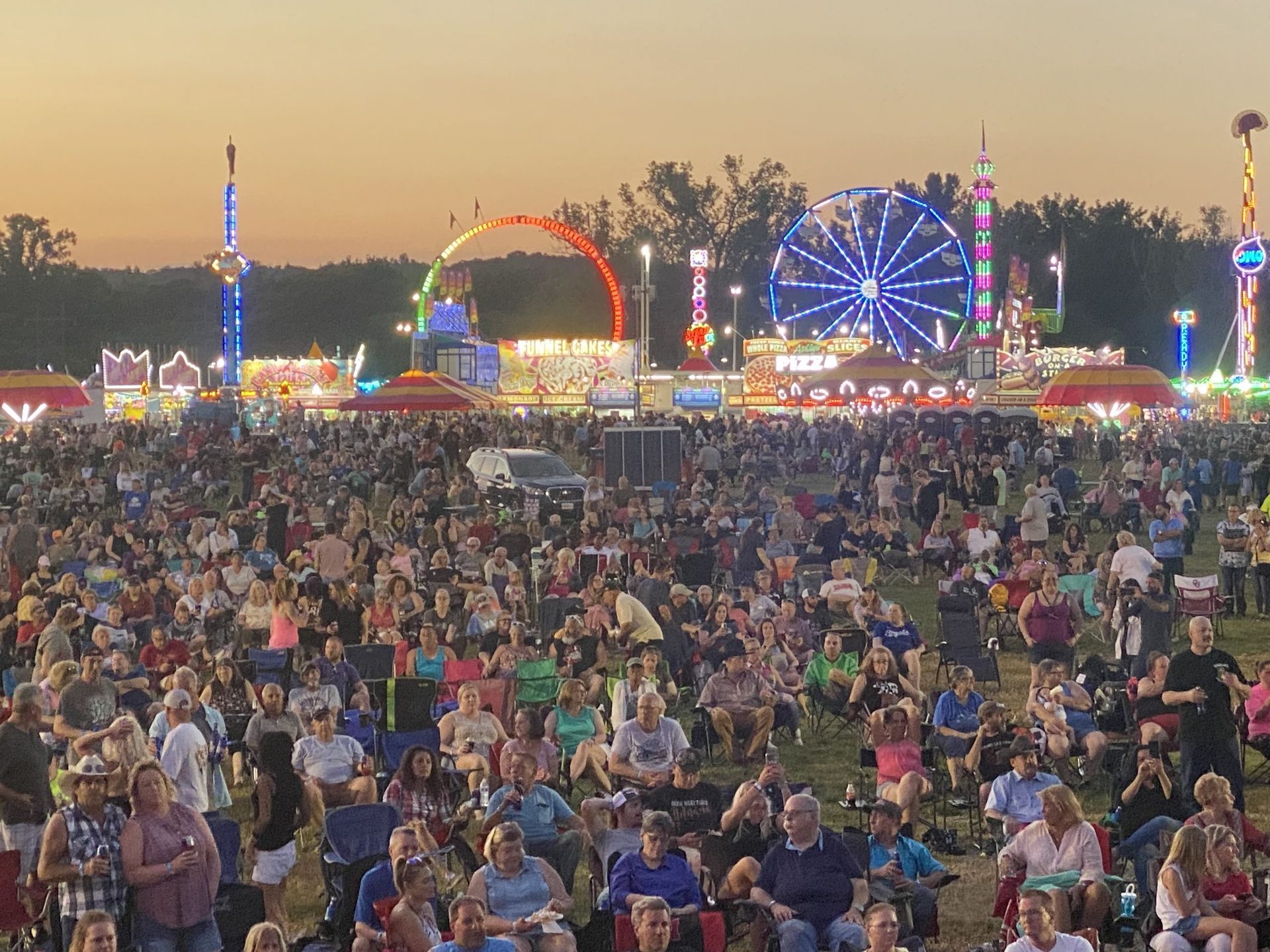 A large crowd of people are sitting in chairs at a carnival.