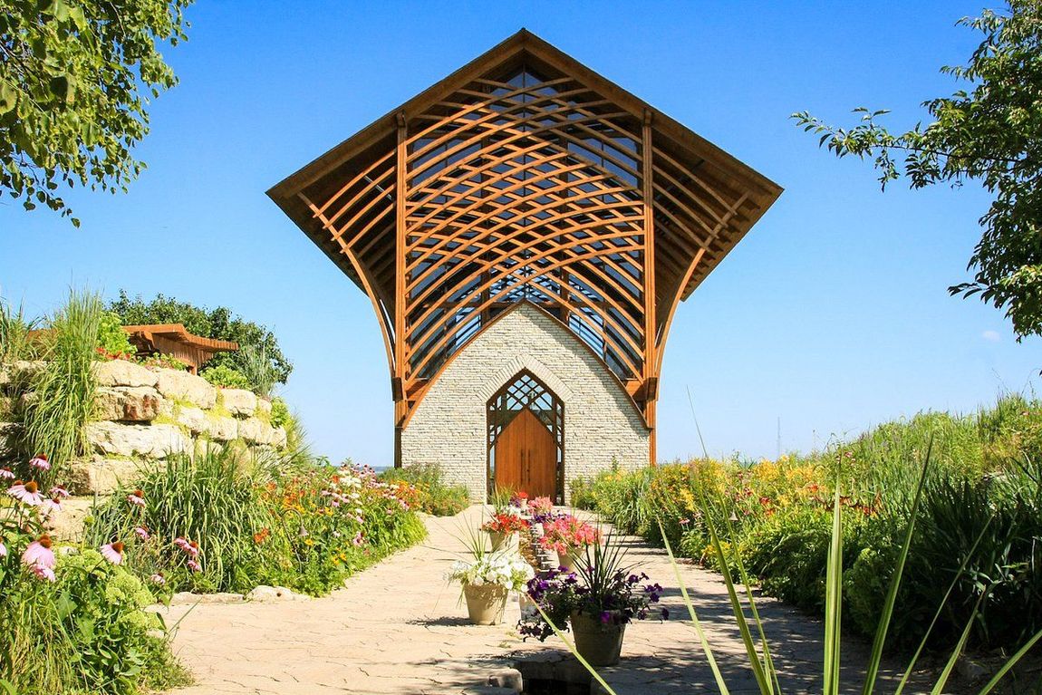 A small church with a wooden roof is surrounded by flowers and trees.