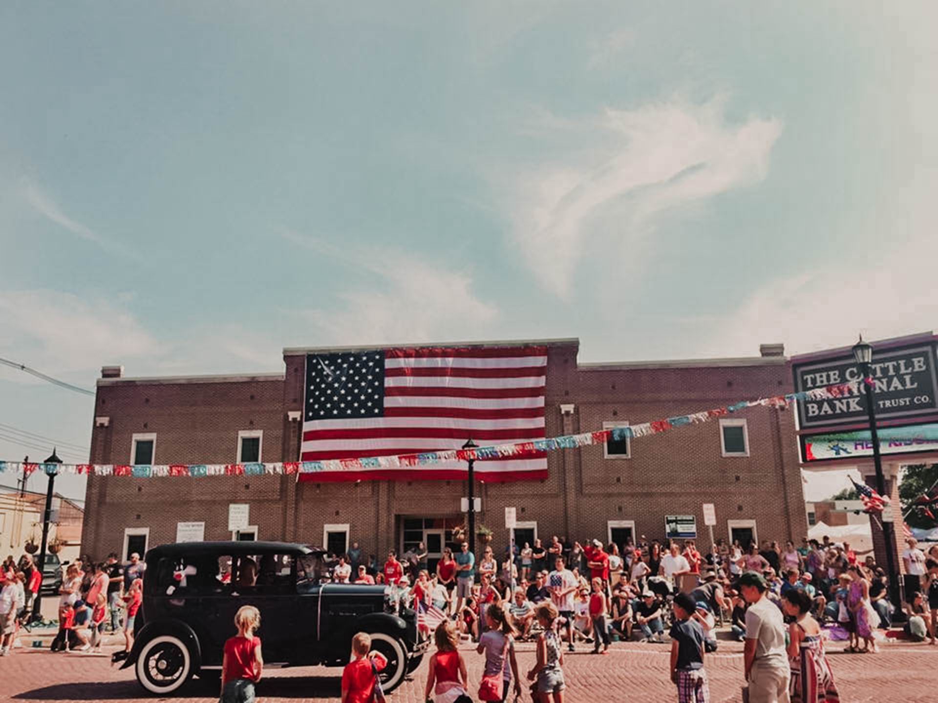 A black car is parked in front of a large american flag.