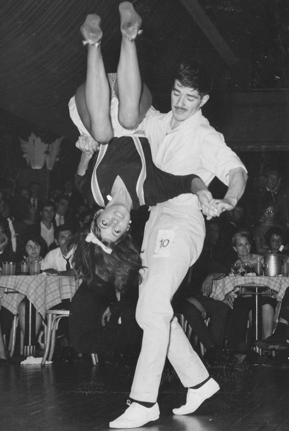 Un homme tient une femme à l'envers sur une piste de danse avec le numéro 10 sur sa chemise