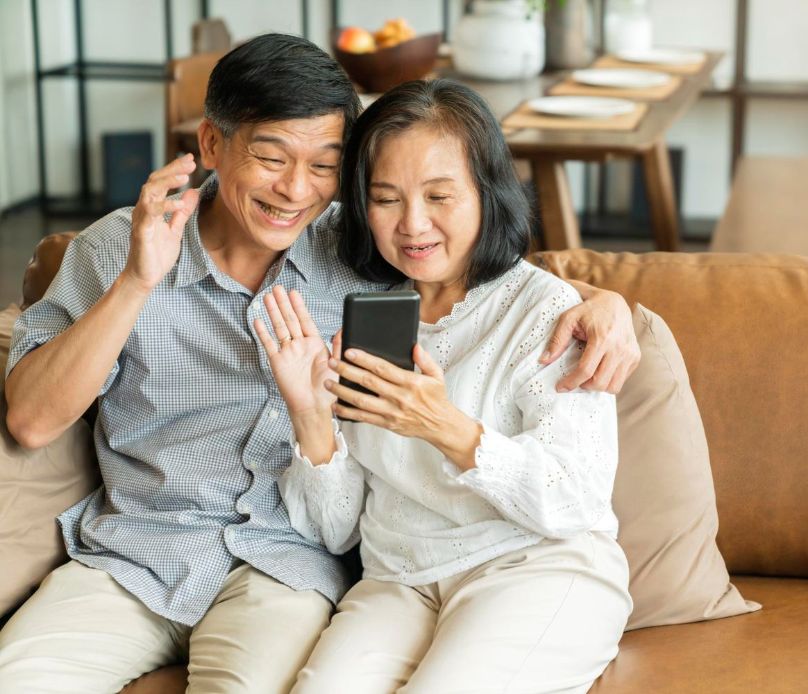 Group of diverse people laughing, gathered around a table with food and a laptop in a bright cafe.