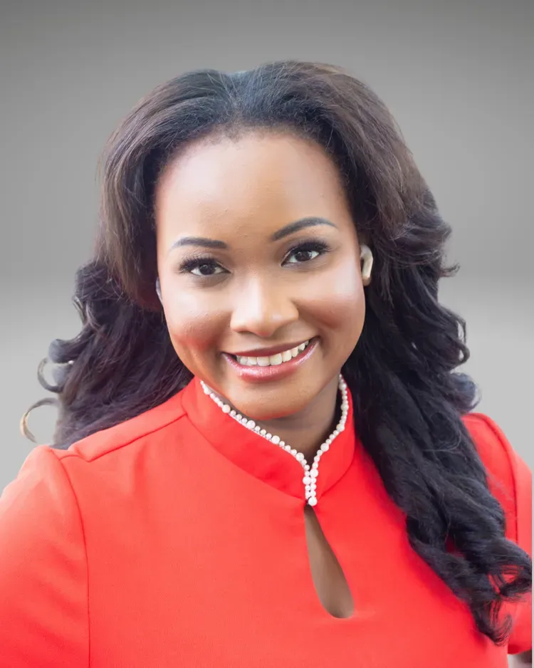 Woman with dark hair smiles, wearing a red top with a keyhole neckline and pearl embellishments.