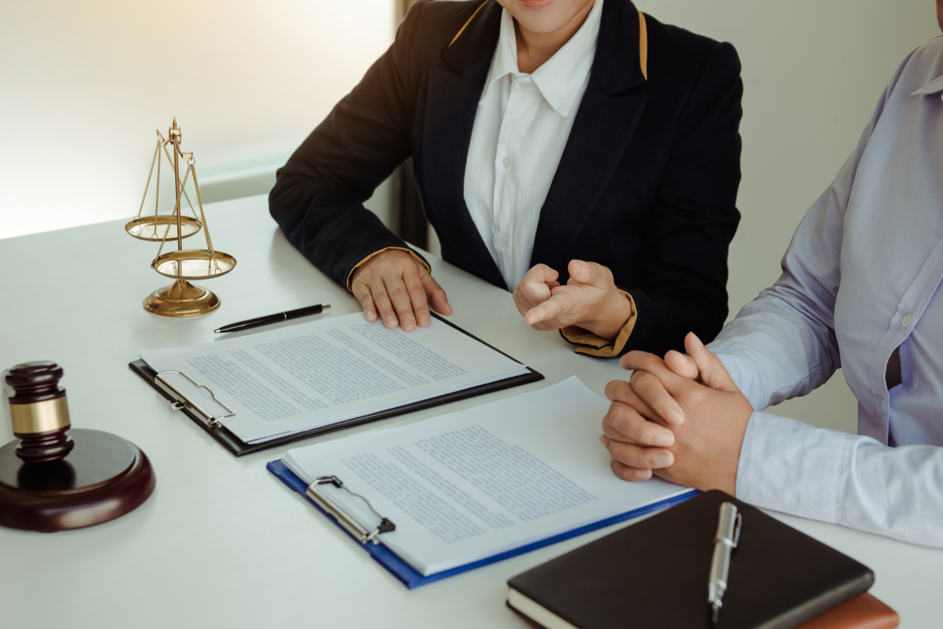 People around a wooden table in a meeting, two shaking hands, laptops and tablets visible.
