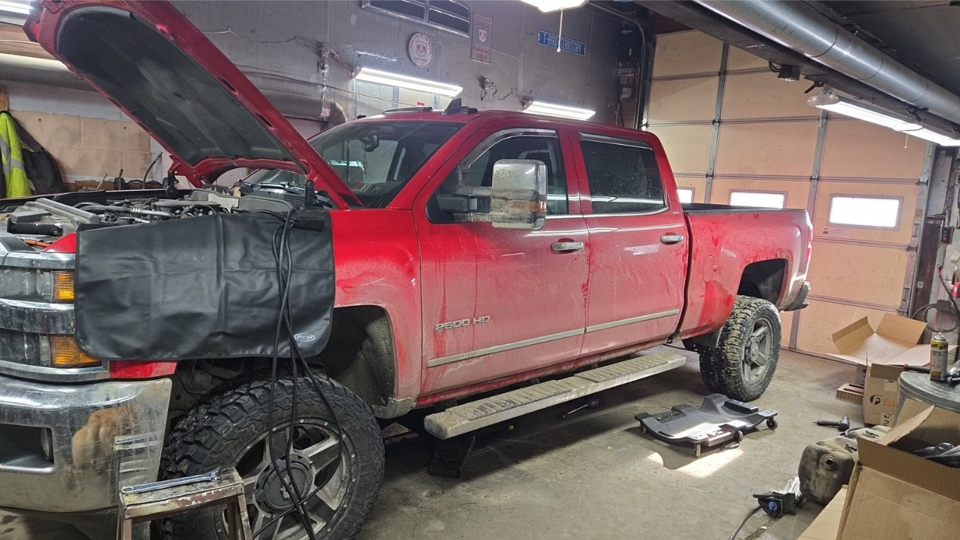 Red pickup truck with the hood open in a garage, possibly undergoing maintenance.