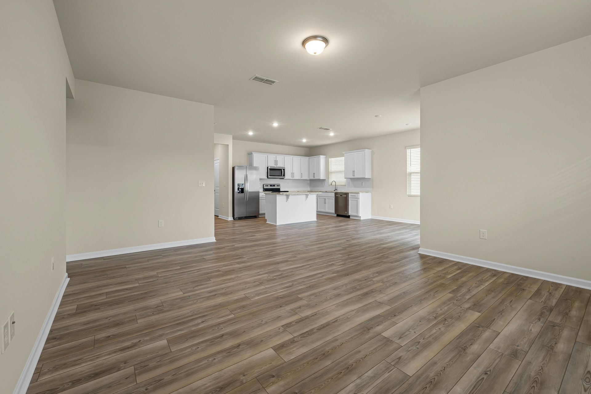 An empty living room with hardwood floors and a kitchen in the background.