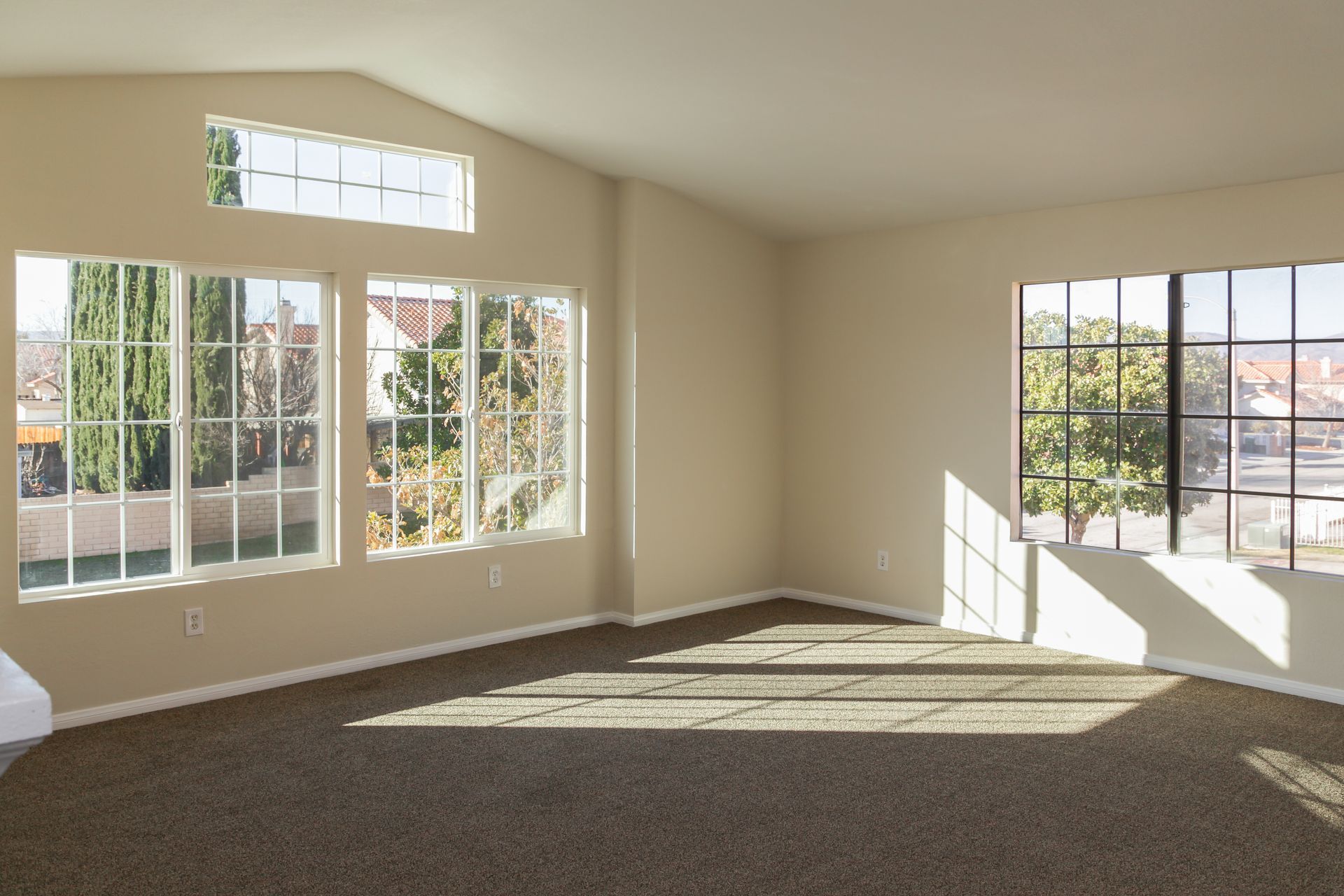 An empty living room with a lot of windows and a brown carpet.
