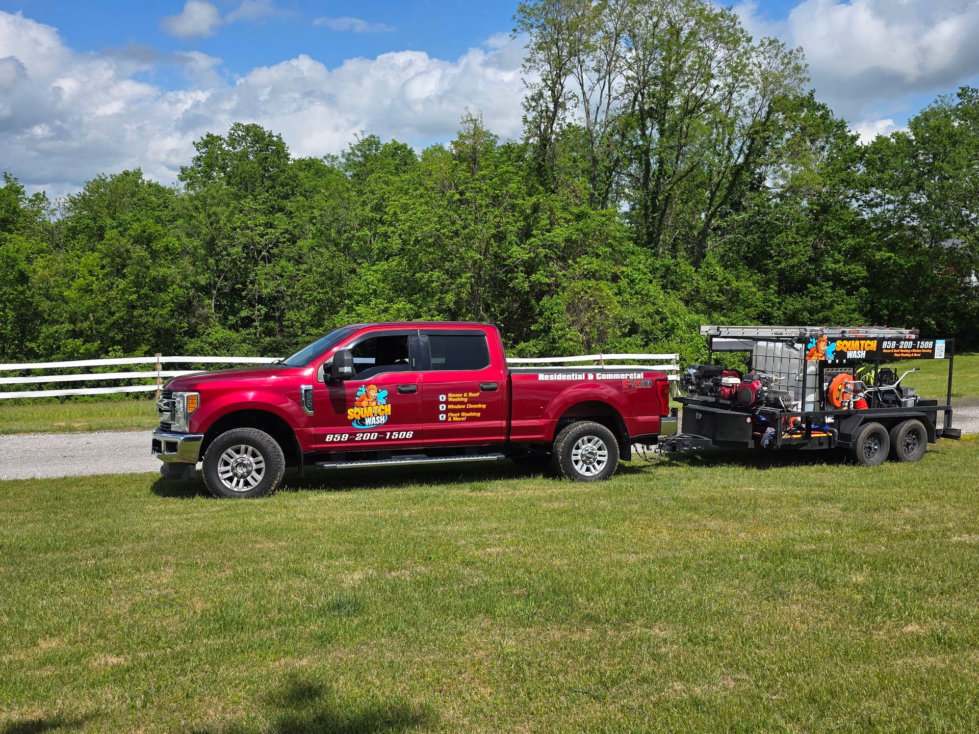 Red pickup truck towing landscaping equipment on a trailer beside a highway, with trees and grass in the background
