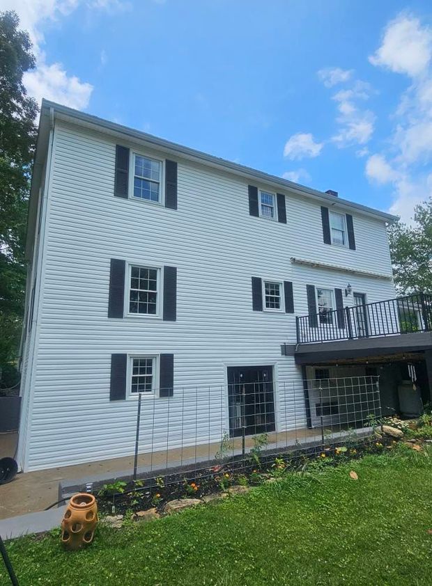 White two-story house with black shutters, a back deck, and a grassy yard under a blue sky.