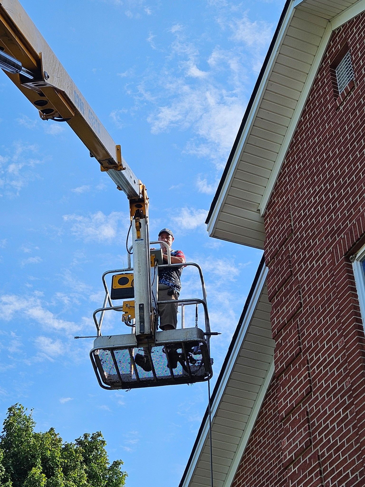 Worker in a lift repairing a brick building's roofline against a blue sky