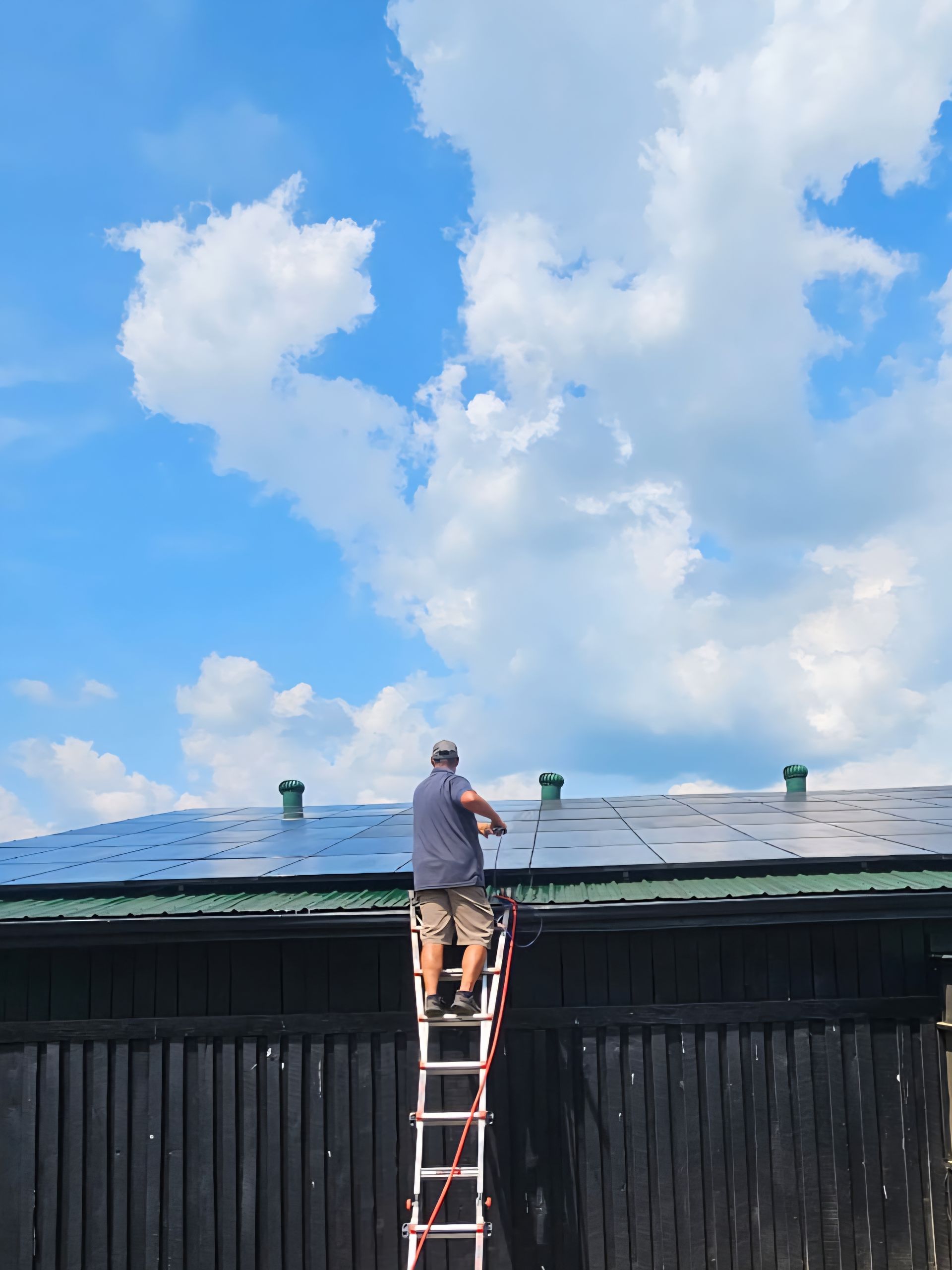 Person standing on a ladder working on a blue roof under a cloudy sky
