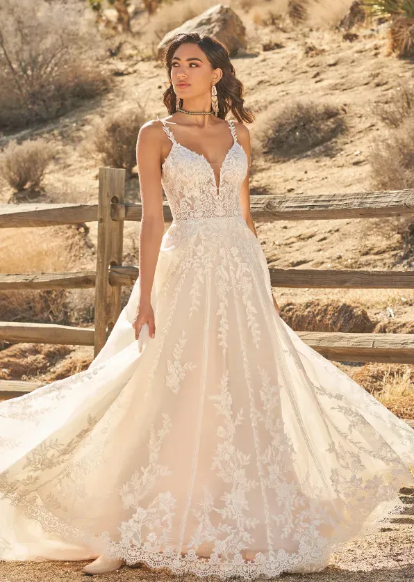 Woman in a white lace wedding dress, outdoors. She's smiling, near a wooden fence.