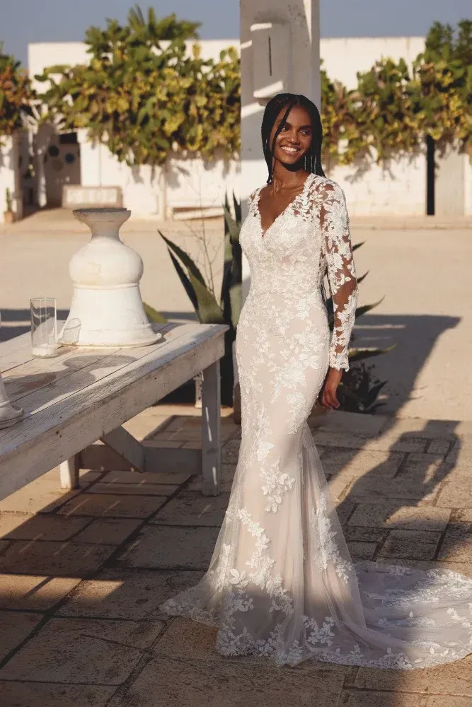 Woman in a white lace wedding dress smiles, outdoors.