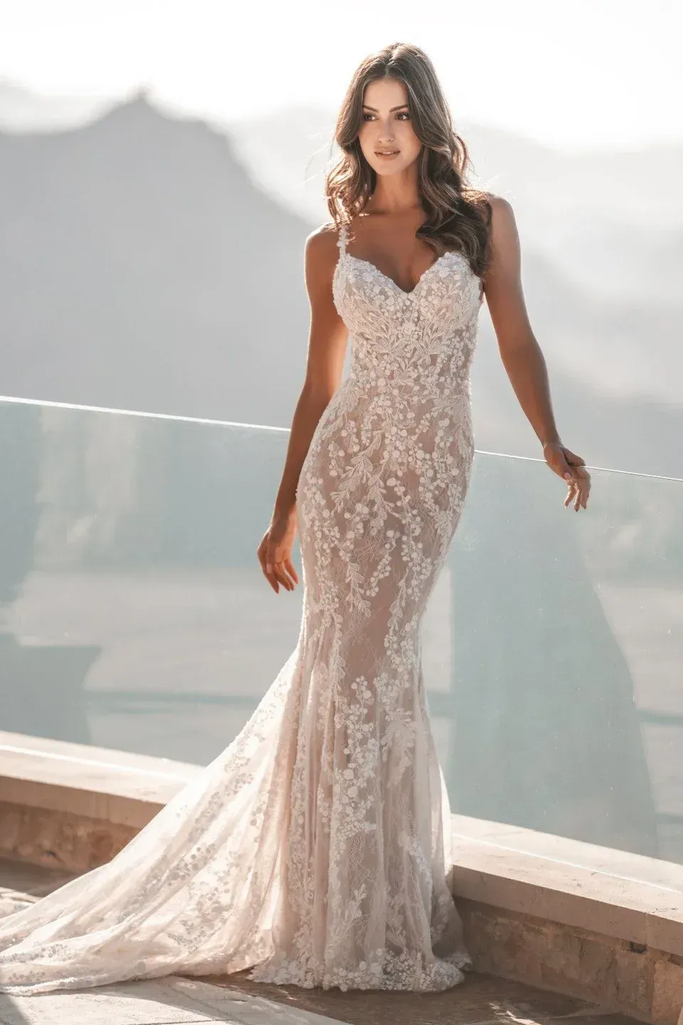 Woman in a white lace mermaid wedding dress posing outdoors on a balcony.