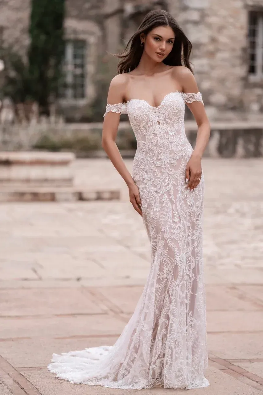Woman in a white off-the-shoulder lace wedding dress, posed outdoors.
