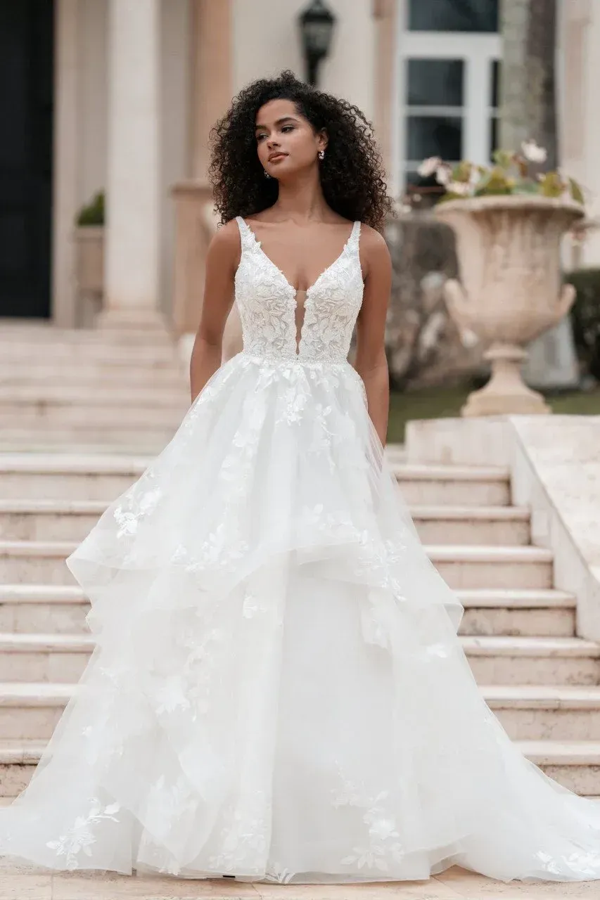 Woman in a white wedding dress with layered skirt, standing on outdoor steps.