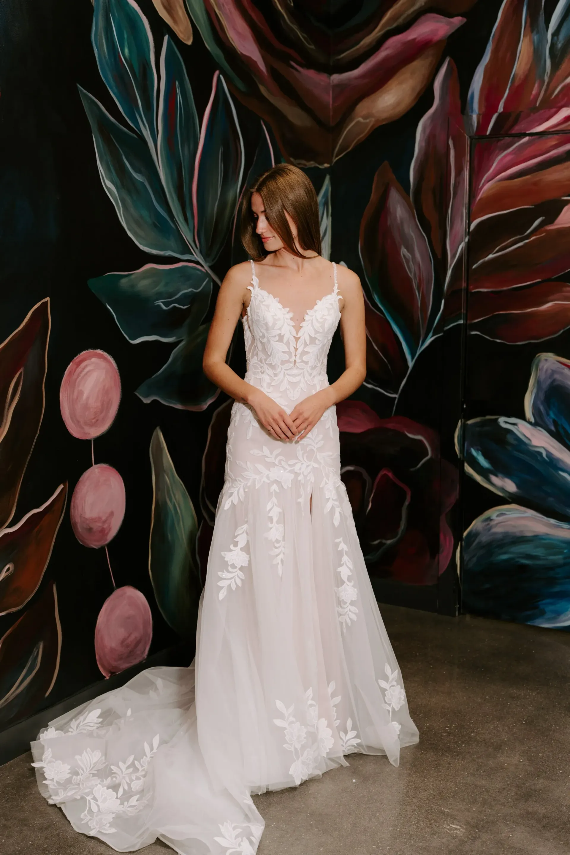 Woman in white wedding dress, posed against a colorful mural.