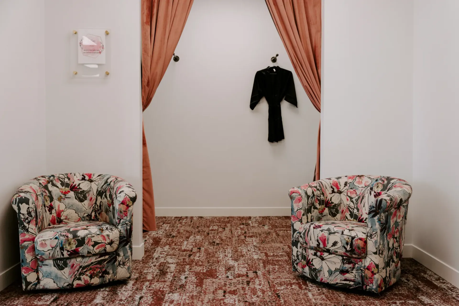 Two floral armchairs face a dressing room with a garment hanging inside.