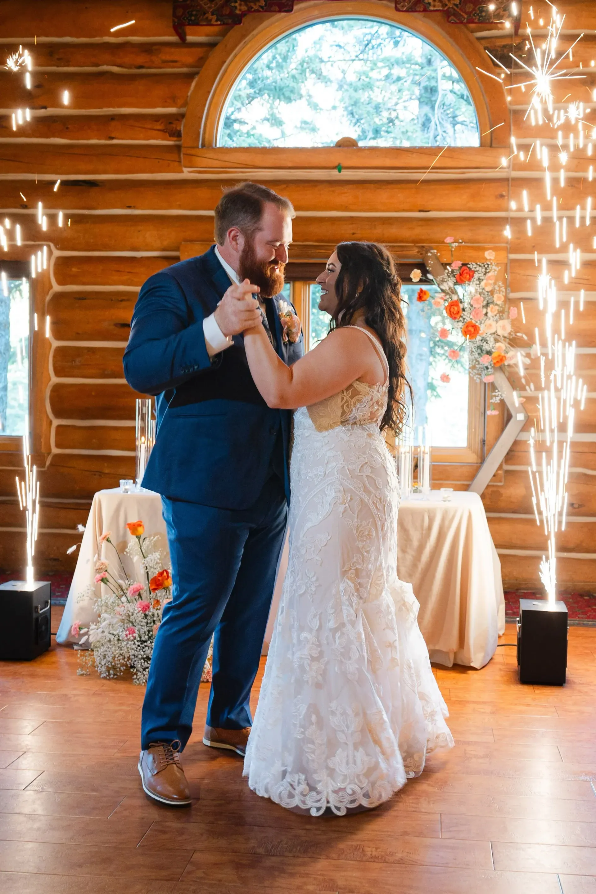 Bride and groom dancing at wedding reception, sparks fly, in front of a wooden backdrop.