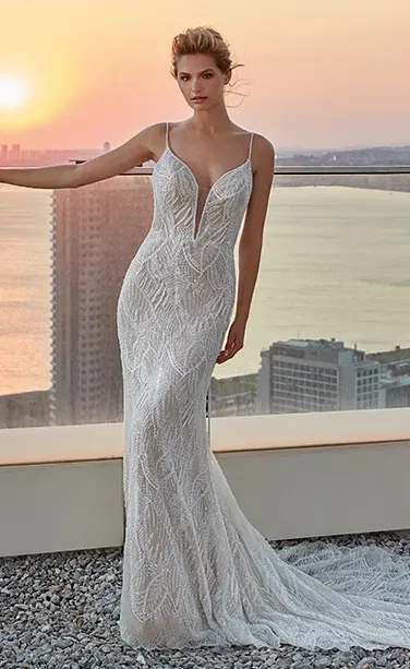 Woman in sparkling white wedding dress with plunging neckline, overlooking cityscape at sunset.