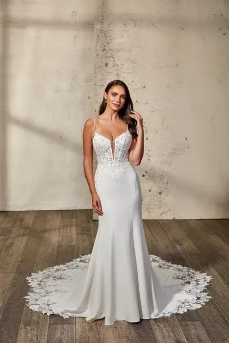 Woman in a white wedding dress with lace detailing, posing in a studio with wooden floor.