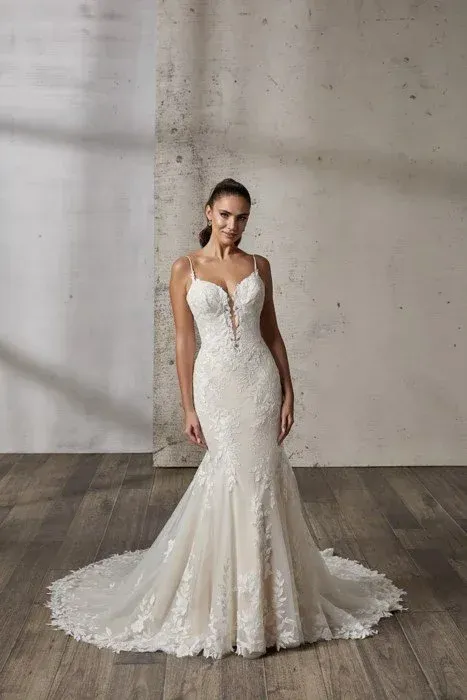 Woman in a white, lace mermaid wedding dress with spaghetti straps, posing indoors.