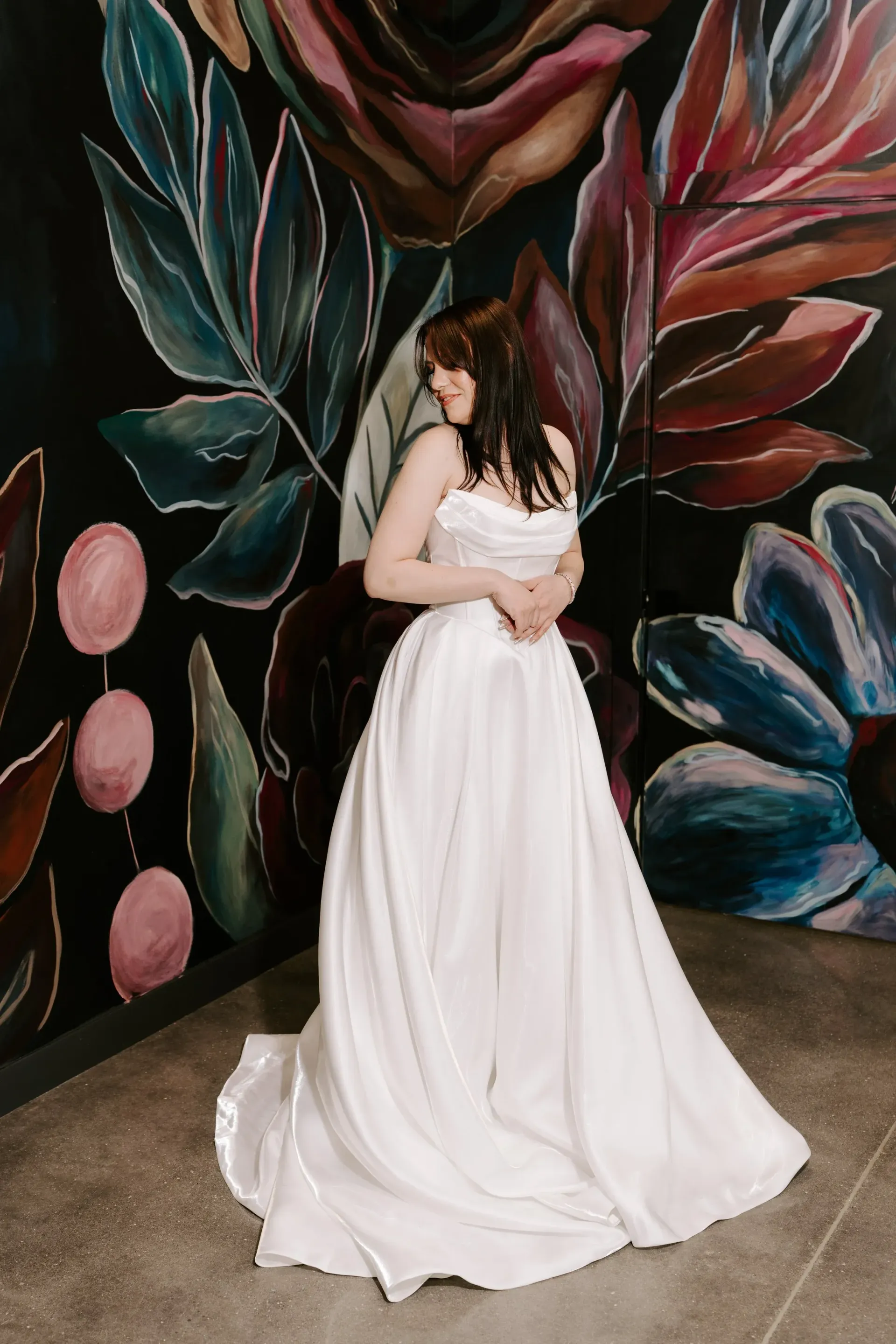 Woman in white wedding dress poses in front of a colorful floral mural.