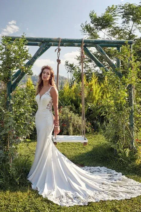 Bride in white wedding dress stands in front of a swing in a garden.