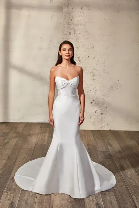 Woman in white strapless mermaid wedding dress, standing, neutral background.